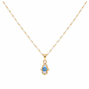 A delicate necklace featuring a gold-tone chain with small white beads and a Hamsa hand pendant. The pendant is detailed with a blue and white evil eye motif and a gold-tone Hamsa hand outline, set against a plain white background.