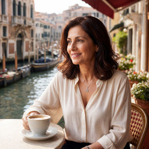 Woman sitting at an outdoor cafe with a view of a canal in Venice, holding a cup of coffee.