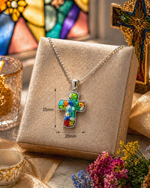Colorful cross pendant necklace on a display card with measurements, surrounded by decorative items.