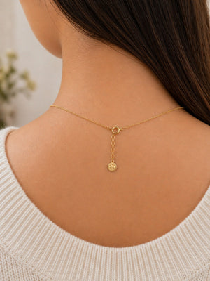Gold necklace on a person wearing a white sweater with a blurred background