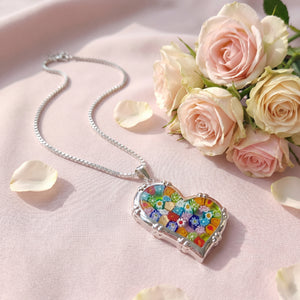 Heart-shaped colorful pendant necklace on a pink surface with roses