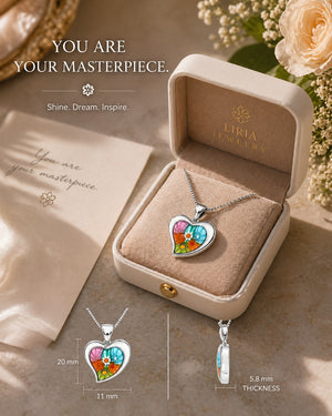Heart-shaped necklace with colorful design in a Liria Jewelry box, surrounded by flowers.