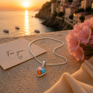 Silver necklace with a heart-shaped pendant on sand with a sunset and coastal background