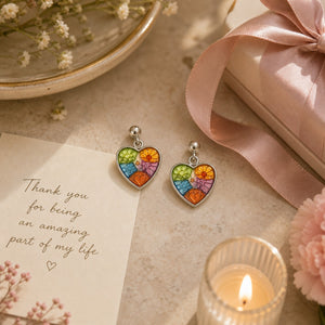 Heart-shaped earrings with colorful design on a surface with a candle and card.