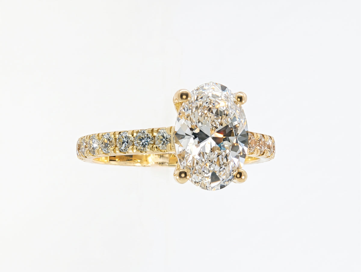 A yellow gold engagement ring featuring a large oval-cut center diamond and a pavé-set diamond band, shown on a clean white background.