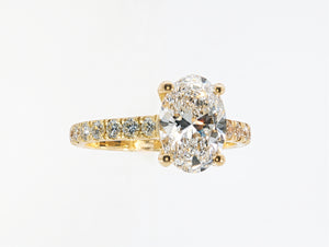 A yellow gold engagement ring featuring a large oval-cut center diamond and a pavé-set diamond band, shown on a clean white background.