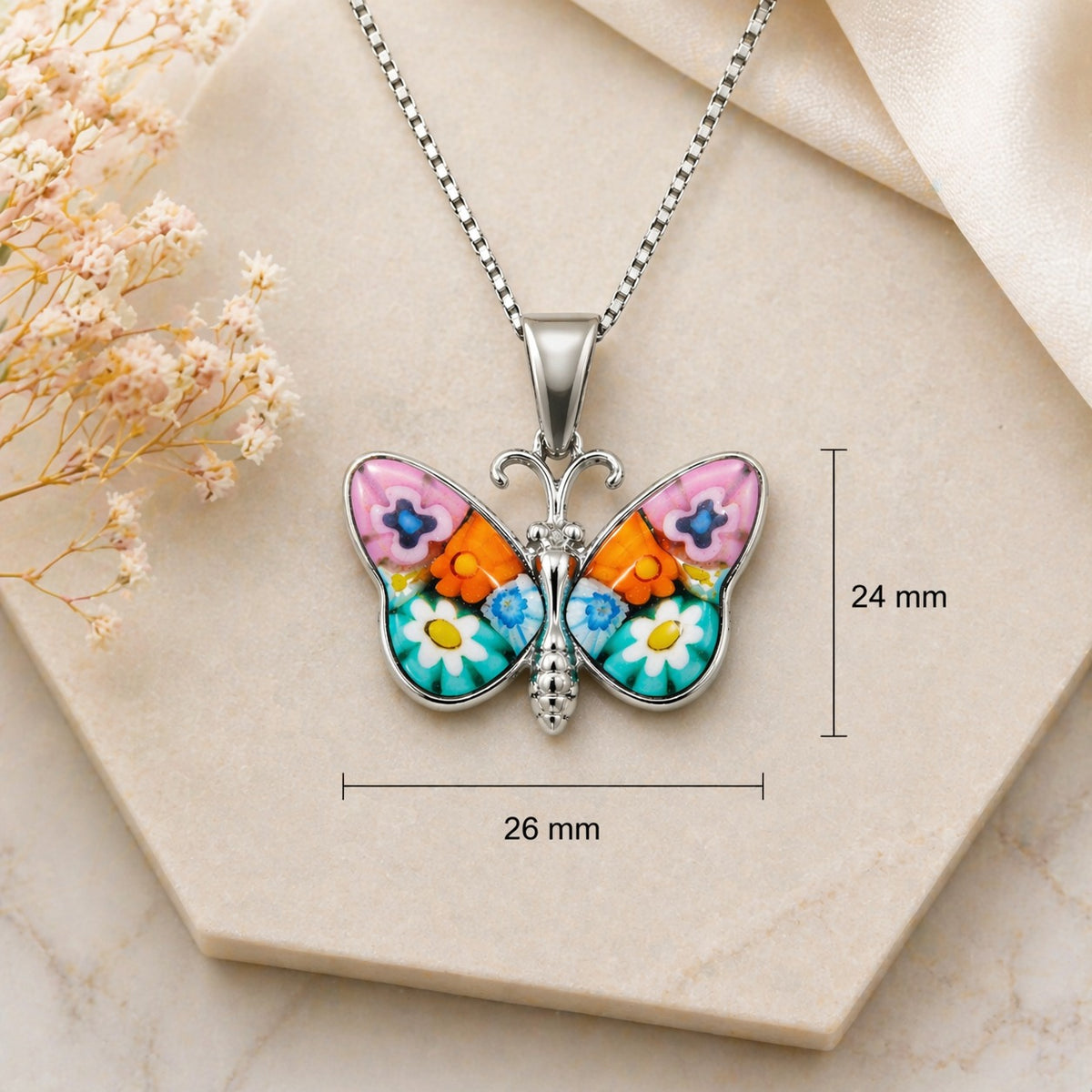 Butterfly-shaped pendant necklace with floral design on a beige surface with measurements.