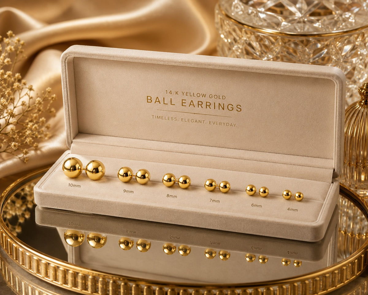 Gold ball earrings in a display case on a reflective surface with gold accents.