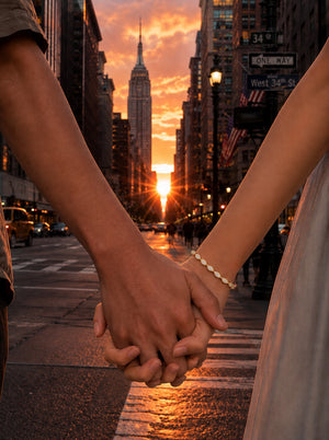 A couple holding hands in the crosswalk of New York City at sunset, with the Empire State Building and a golden street scene in the background.