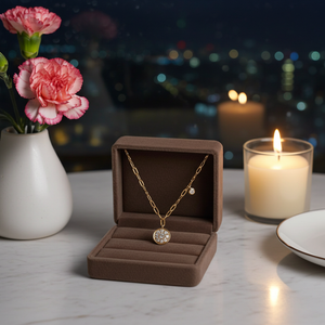 Gold necklace in a brown jewelry box with pink flowers and candles in the background