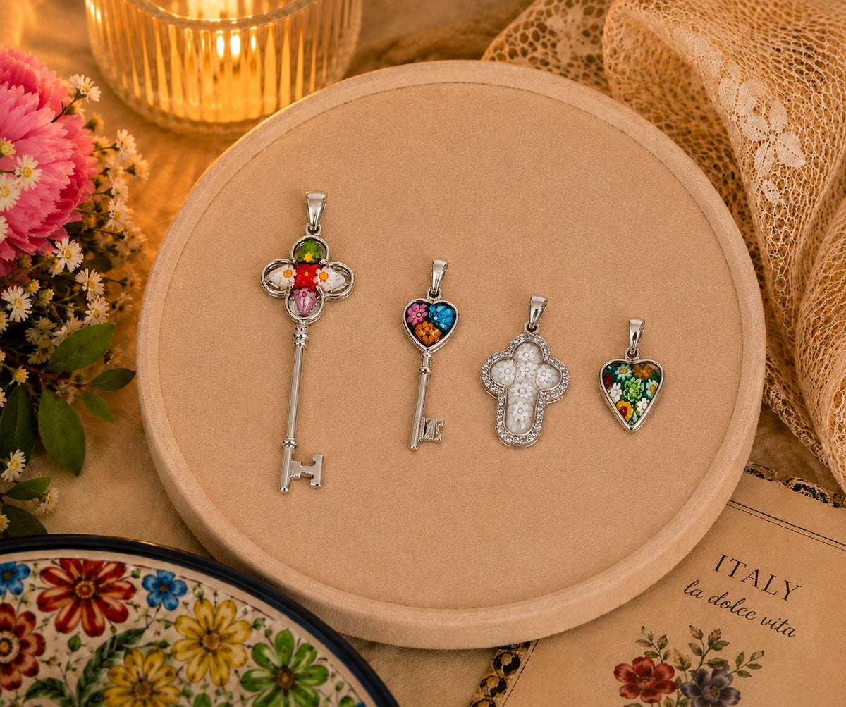 Four silver pendants on a round beige display with flowers and a candle in the background.