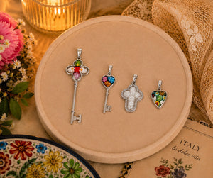 Four silver pendants on a round beige display with flowers and a candle in the background.
