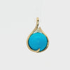 A gold teardrop pendant featuring a large, smooth round turquoise cabochon and a small cluster of clear accent stones at the top, set against a clean white background.