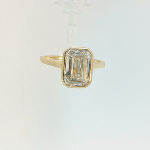A yellow gold ring featuring a large rectangular emerald-cut clear gemstone in a bezel setting, shown against a plain white background.