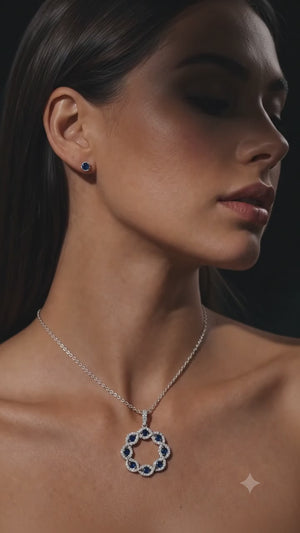 A luxurious Liria Jewelry set crafted in genuine 14K white gold, featuring an elegant pendant necklace and matching stud earrings adorned with deep blue gemstones, beautifully displayed on a dark marble surface beside a sophisticated black Liria Jewelry jewelry box.
