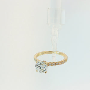 A yellow gold solitaire engagement ring featuring a large round brilliant-cut center stone, with a pavé-set band adorned with smaller round diamonds, shown on a clean white background.