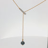 A gold Y-necklace featuring a horizontal bar pavé-set with clear stones and a dangling beaded chain ending in a round black gemstone pendant, shown on a plain white background.