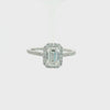 An emerald-cut halo ring featuring a central baguette diamond surrounded by a double halo of smaller round diamonds, with a pavé-set band in a silver-colored metal, shown on a plain white background.