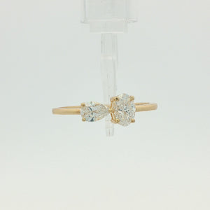 A yellow gold ring featuring a pear-cut diamond on the left and a round brilliant-cut diamond on the right, set on a polished gold band against a clean white background.