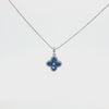 A 14K white gold bead chain necklace featuring a four-leaf clover pendant set with four vivid blue diamonds, accented by a sparkling halo of round white diamonds and a diamond cluster at the center, displayed on a clean white studio background.