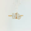A yellow gold ring featuring an emerald-cut diamond on the left and a pear-cut diamond on the right, set against a plain white background.
