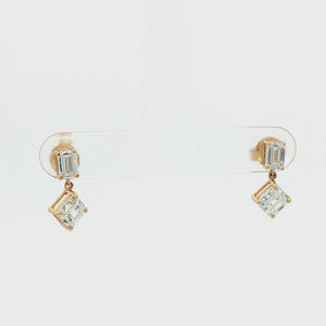 A pair of gold drop earrings featuring a rectangular baguette-cut clear gemstone in the top setting and a larger square princess-cut clear gemstone in the bottom setting, shown on a clean white background.