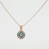 Liria Jewelry Evil Eye Necklace displayed in an open cream-colored presentation box, with product text and decorative elements on a warm beige background.