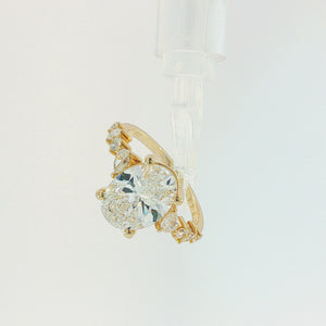 A yellow gold ring featuring a large oval-cut diamond center stone with smaller round and marquise-cut diamonds set along the shoulders, shown on a plain white background.