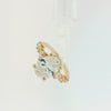 A yellow gold ring featuring a large oval-cut diamond center stone with smaller round and marquise-cut diamonds set along the shoulders, shown on a plain white background.