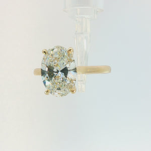 An oval-cut diamond engagement ring with a yellow gold band, shown on a clean, light gray background.