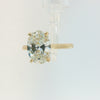 An oval-cut diamond engagement ring with a yellow gold band, shown on a clean, light gray background.