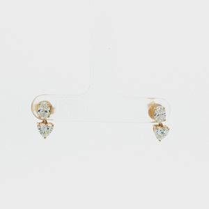 A pair of gold drop earrings featuring a round brilliant-cut diamond at the top and a heart-shaped diamond below, set in yellow gold on a white background.