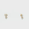 A pair of gold drop earrings featuring a round brilliant-cut diamond at the top and a heart-shaped diamond below, set in yellow gold on a white background.