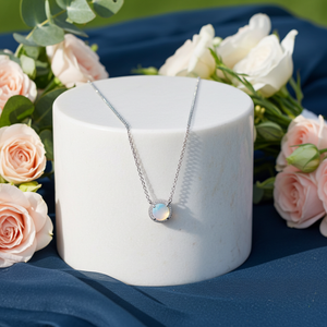 Necklace with a pendant on a white stand surrounded by pink roses on a blue fabric background