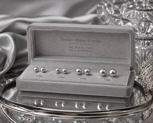 Silver ball earrings in a display case with 'Timeless. Elegant. Everyday.' text on a reflective surface.